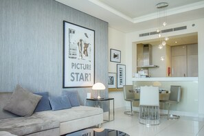 A modern living room with a sofa, a coffee table, and a dining area with chairs and a kitchen in the background.