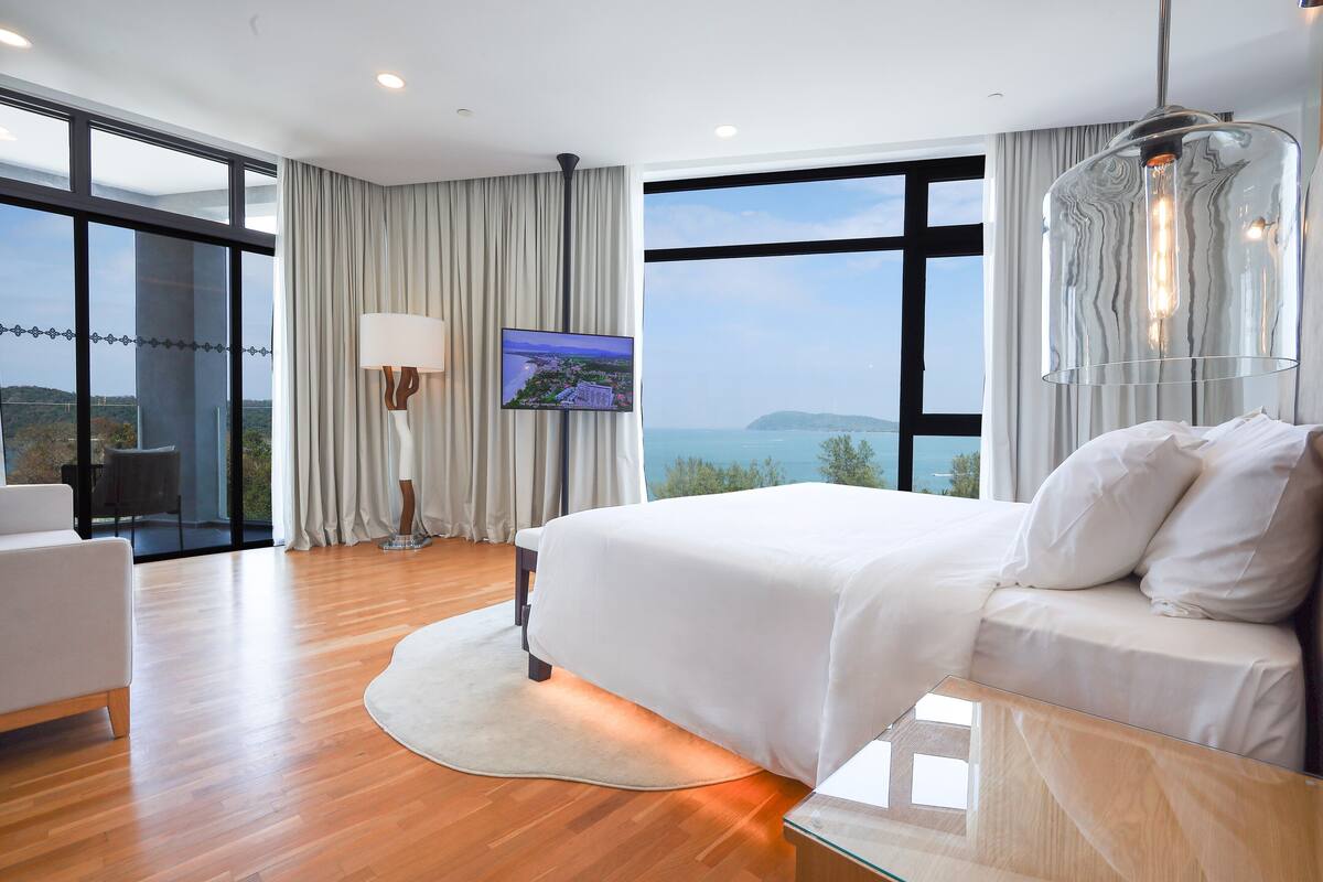 A modern hotel room with a large bed, a flat-screen TV, and a view of the sea.