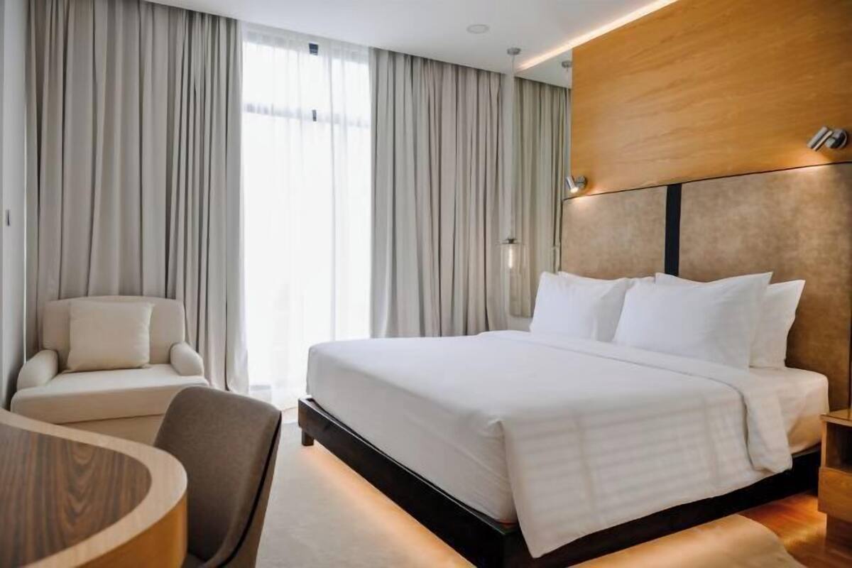 A hotel room with a bed, a chair, a table, and curtains.