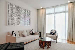 Una sala de estar moderna con sofá, sillones, una mesa de centro de vidrio y una gran obra de arte mural con letras del alfabeto.