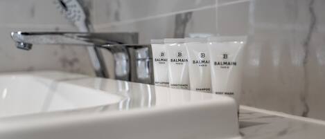 Un baño con un lavabo blanco, un grifo moderno y varios productos de cuidado de la piel Balmain Paris.