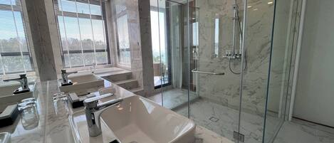 A modern bathroom with a large marble sink, a glass shower enclosure, and a view of the outdoors.