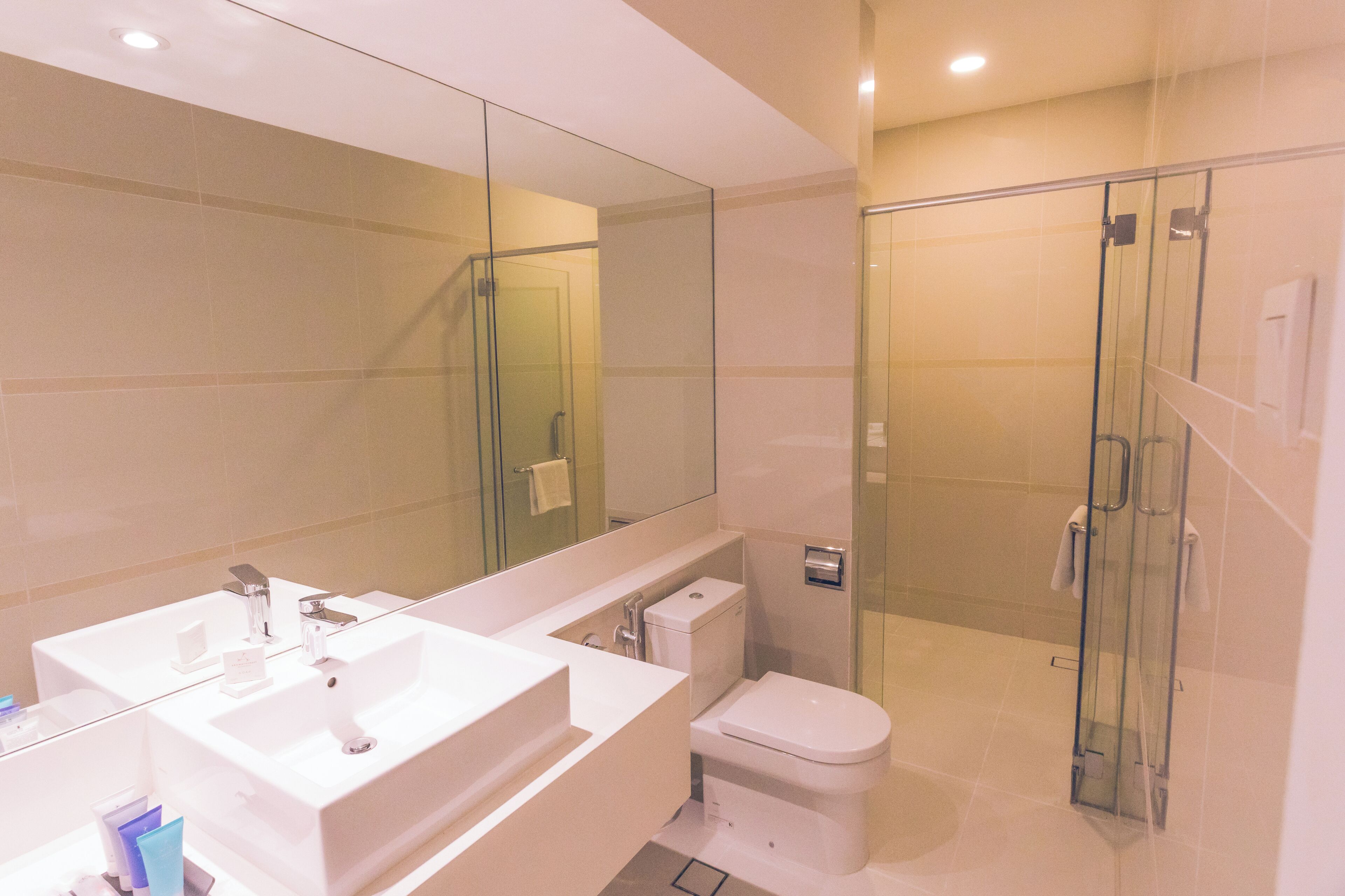 A modern bathroom with a large mirror, two sinks, a toilet, and a glass-enclosed shower area.