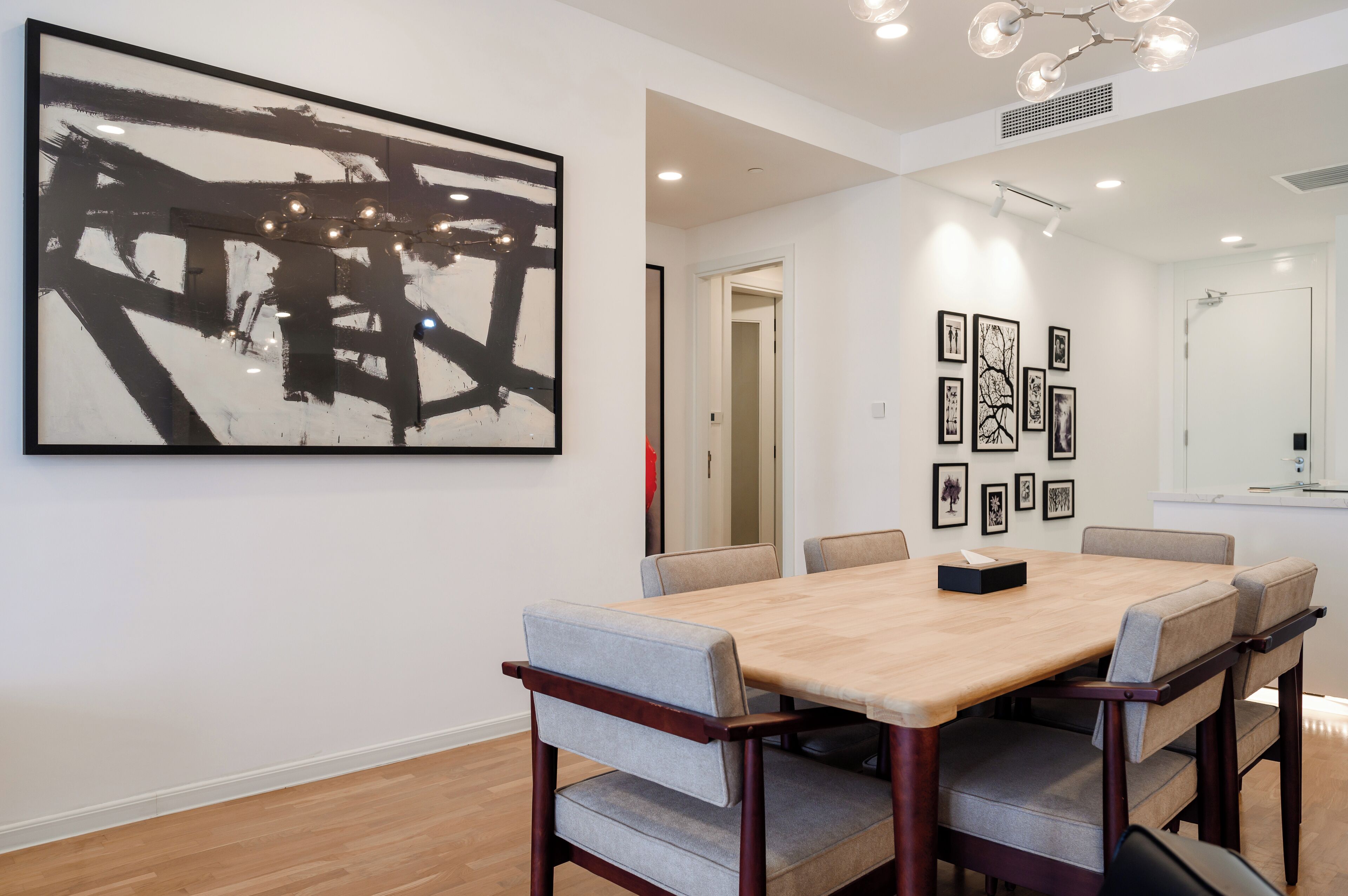 Un comedor moderno con una mesa de madera y sillas acolchadas, un cuadro abstracto grande y fotografías enmarcadas en la pared.