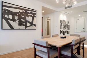 Un comedor moderno con una mesa de madera y sillas acolchadas, un cuadro abstracto grande y fotografías enmarcadas en la pared.