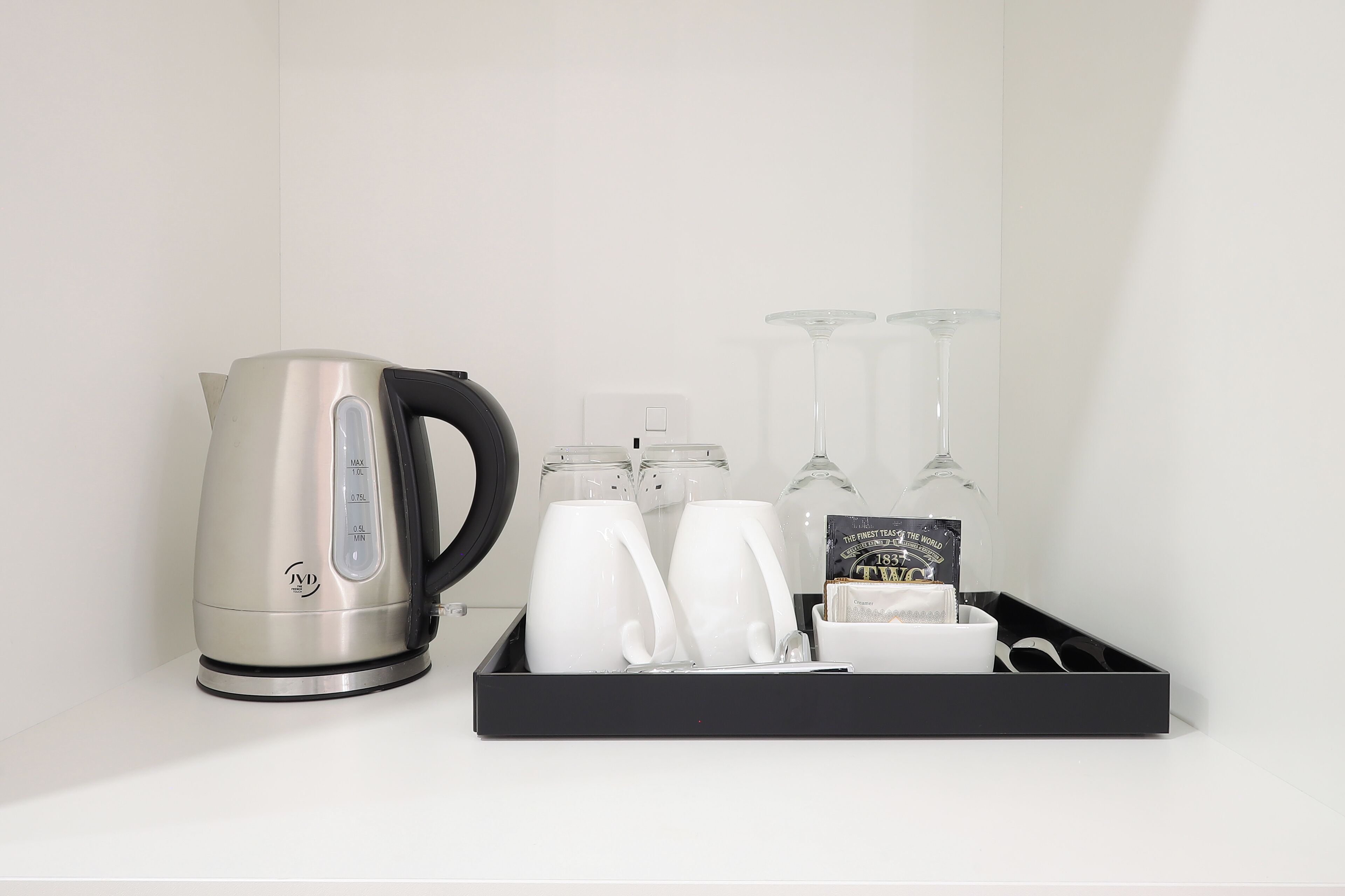 Una cocina con hervidor, dos tazas blancas, tres copas de vino y una bandeja con juego de té y un libro.