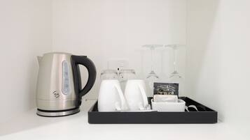 Una cocina con hervidor, dos tazas blancas, tres copas de vino y una bandeja con juego de té y un libro.