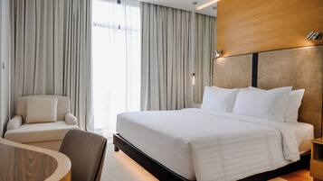 A hotel room with a large bed, a sofa, a chair, and a wooden table.