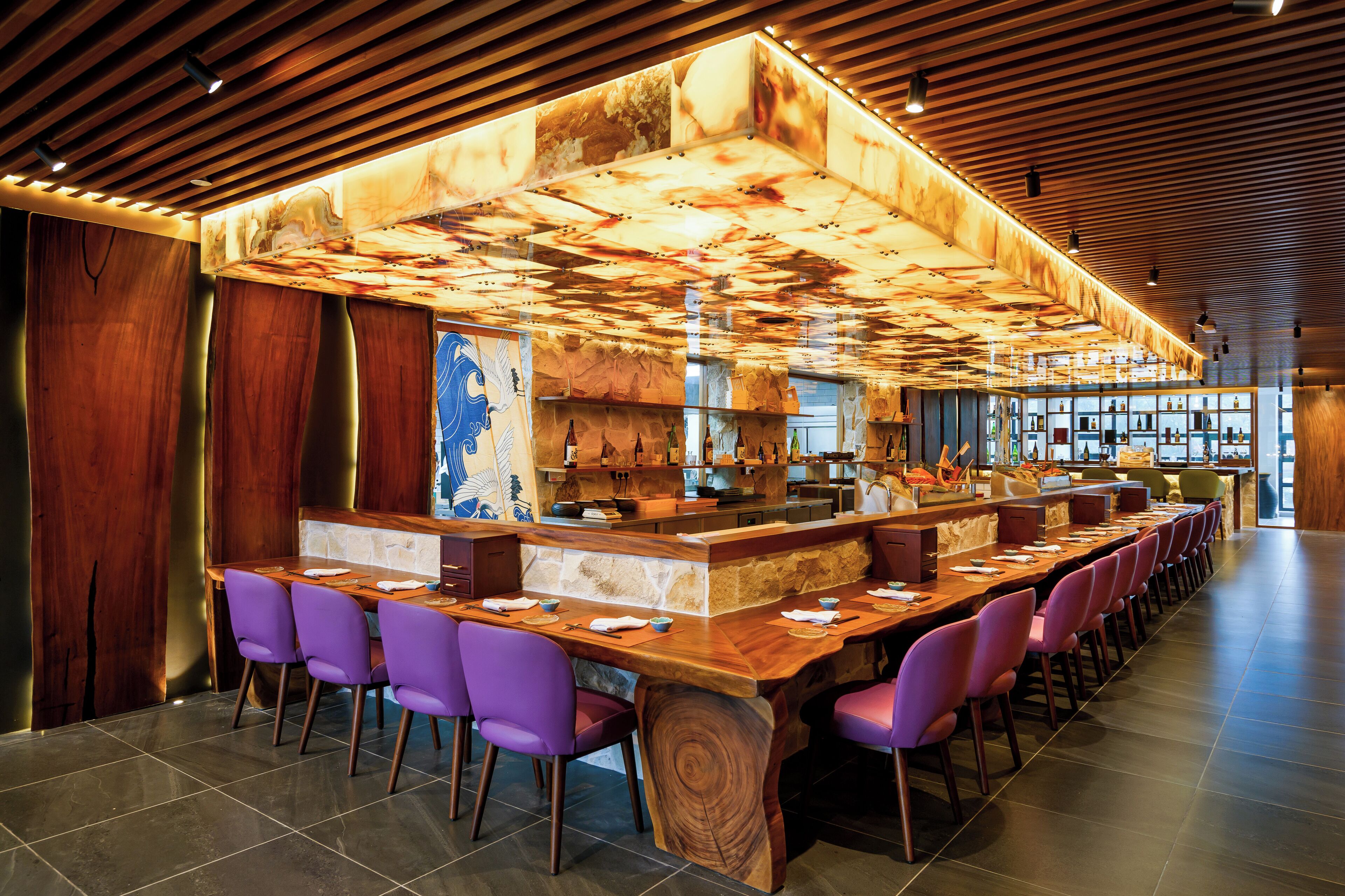 A modern bar with a wooden ceiling and a long counter with purple chairs.