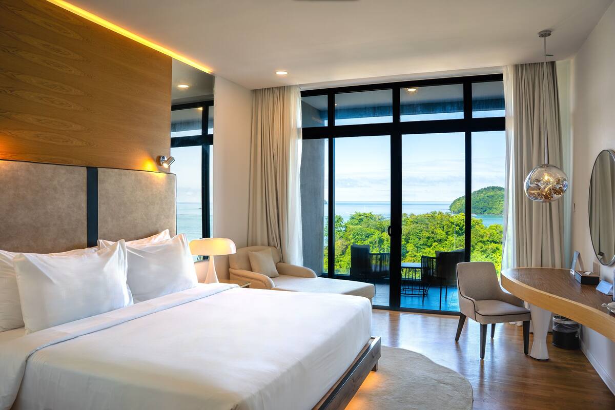 A modern hotel room with a large bed, a desk, and a view of the outdoors.