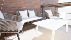 Eine Terrasse mit Korbmöbeln, einem weißen Tisch und einer Ziegelwand.