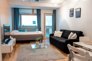 A modern living room with a bed, a black sofa, a glass coffee table, and a TV. - 2ndhomes Deluxe Studio w Sauna & Balcony (Helsinki)