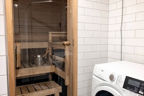 A laundry room with a washing machine, wooden shelves, and a shower enclosure.