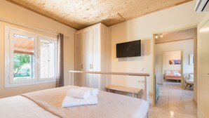 A well-lit bedroom with a large bed, a wooden wardrobe, a television mounted on the wall, and a view of the outside through a window. - Amygdalia Villa (Zakynthos)