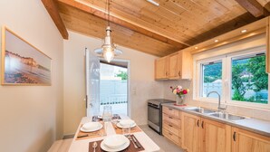 A modern kitchen with wooden cabinets, a dining table set for four, and a large window with a view of greenery. - Amygdalia Villa (Zakynthos)