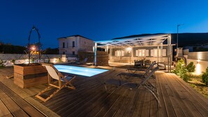 A wooden deck with a pool, lounge chairs, and a covered patio area with seating. - Amygdalia Villa (Zakynthos)