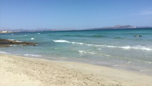Una platja amb aigua cristal·lina, sorra daurada i muntanyes a la distància.