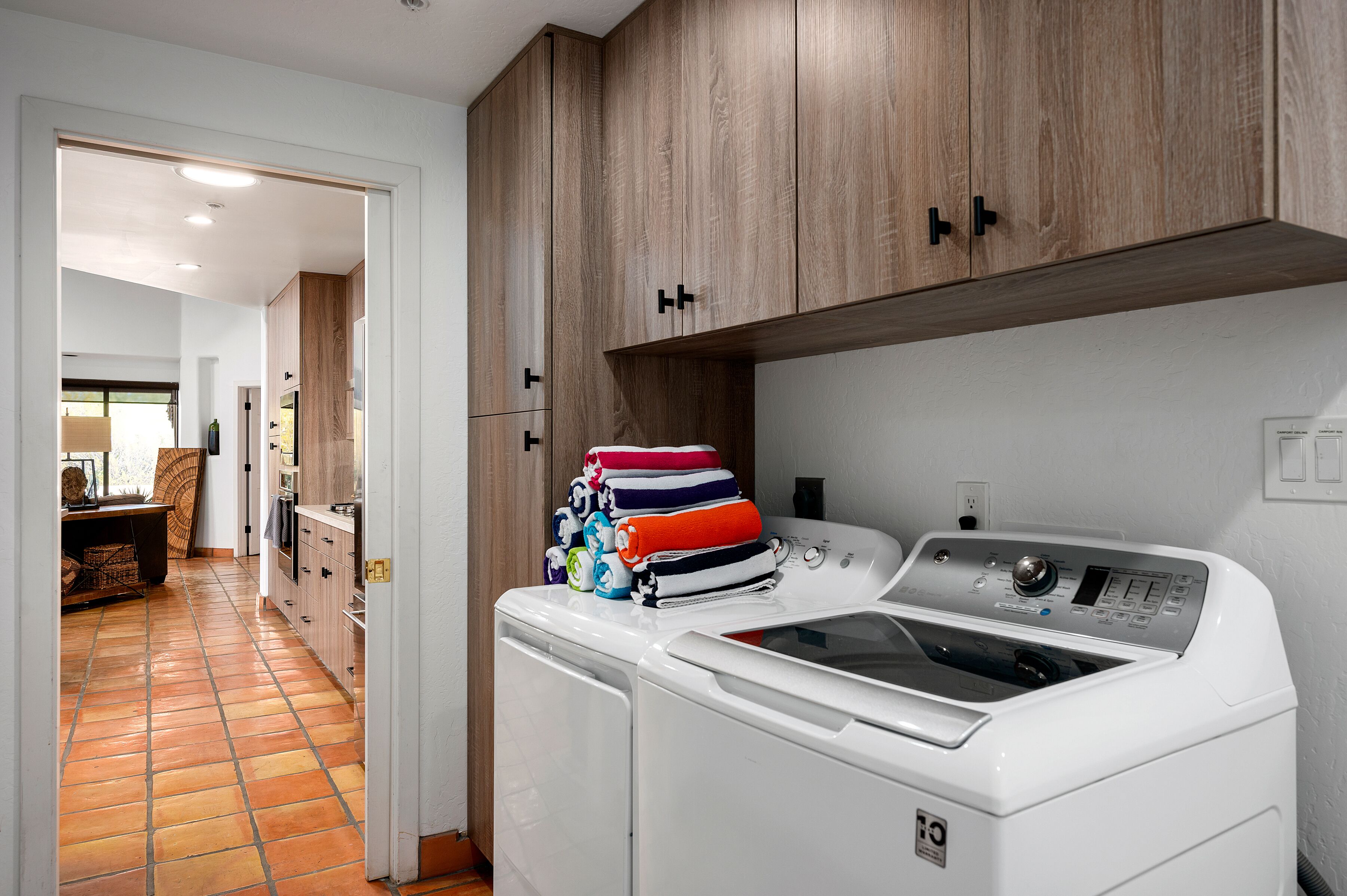 A laundry room with a stacked washer and dryer, wooden cabinets, and a tiled floor.