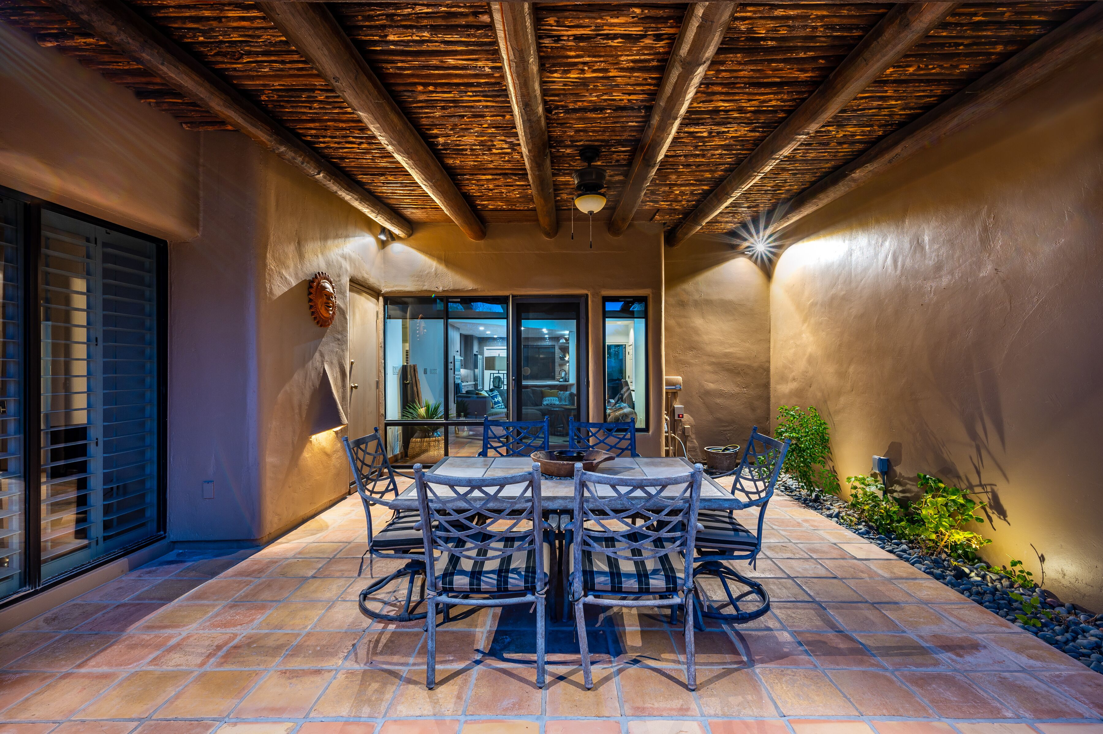 Un patio al aire libre con suelo de baldosas, techo de madera y una mesa de comedor con sillas.
