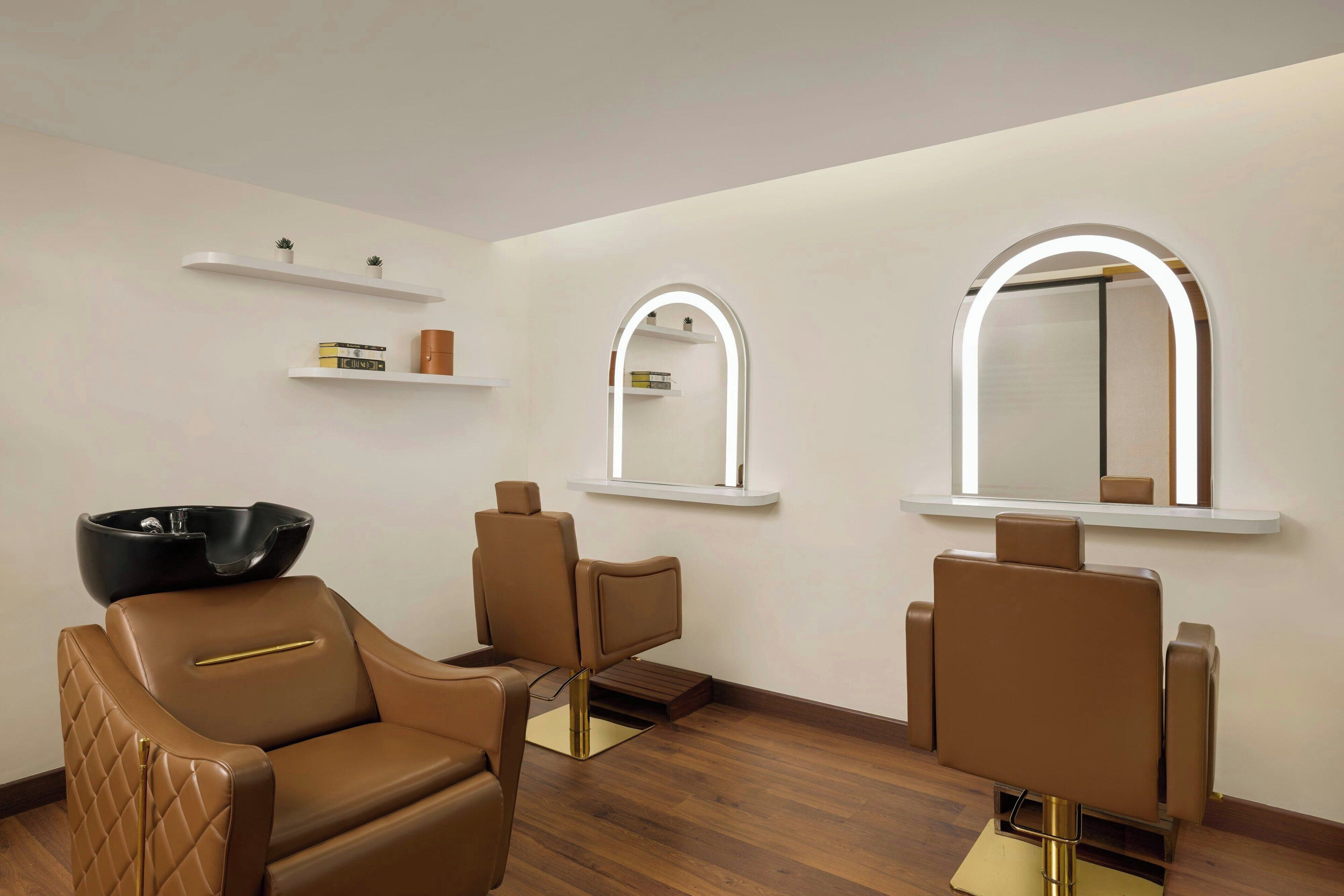Un salon moderne avec trois fauteuils en cuir, un lavabo noir et deux miroirs éclairés fixés au mur.