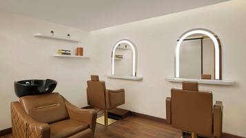 Un salon moderne avec trois fauteuils en cuir, un lavabo noir et deux miroirs éclairés fixés au mur.