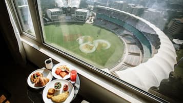 Una mesa de comedor con platos de comida y un vaso de jugo, con vista a un estadio.