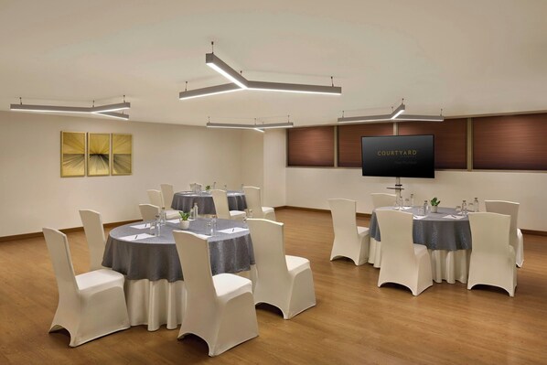 A conference room with round tables, white chairs, and a flat-screen TV displaying "Courtyard Mumbai".
