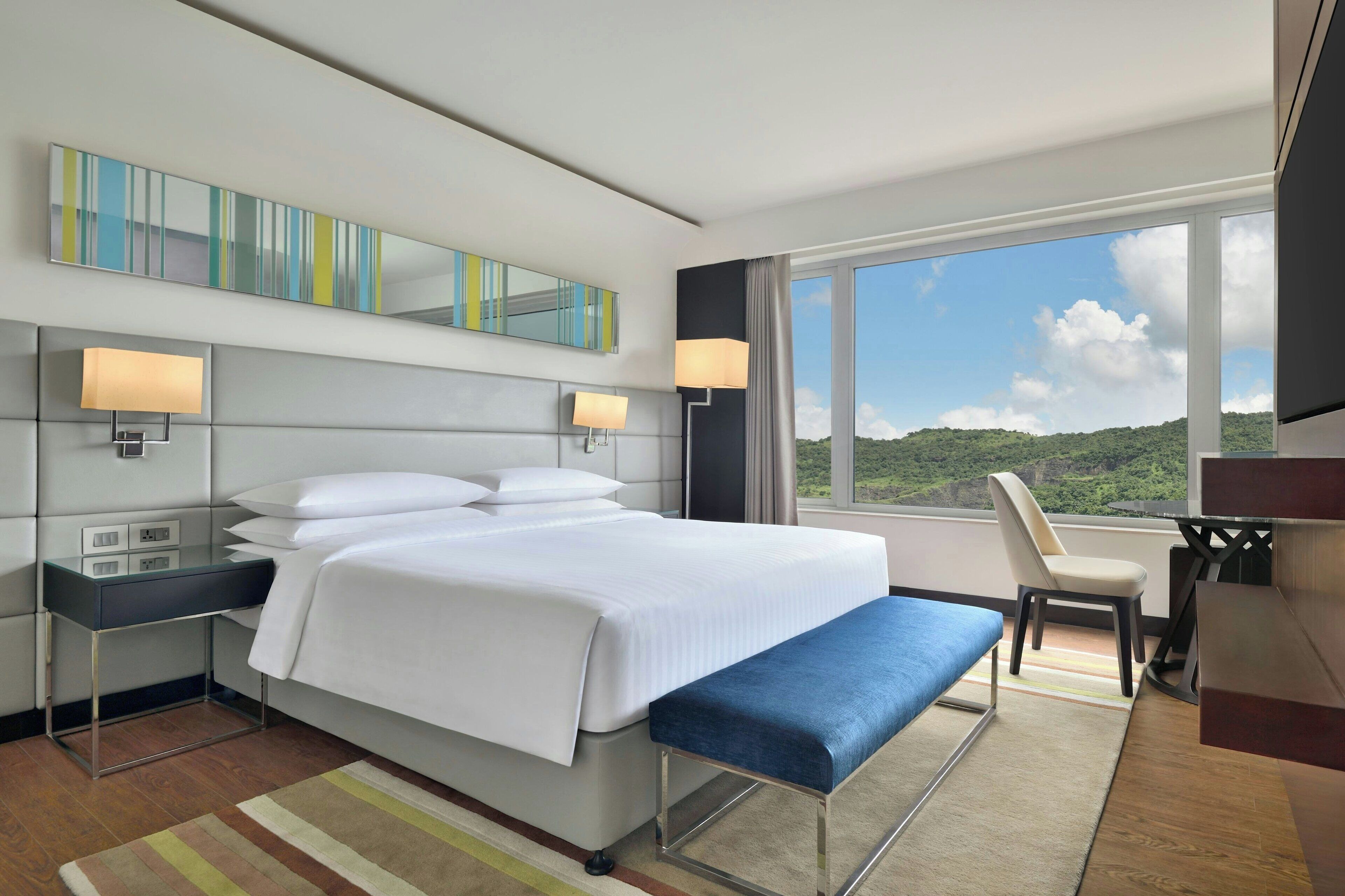 Een moderne hotelkamer met een groot bed, nachtkastjes, een bureau en uitzicht op de omgeving.