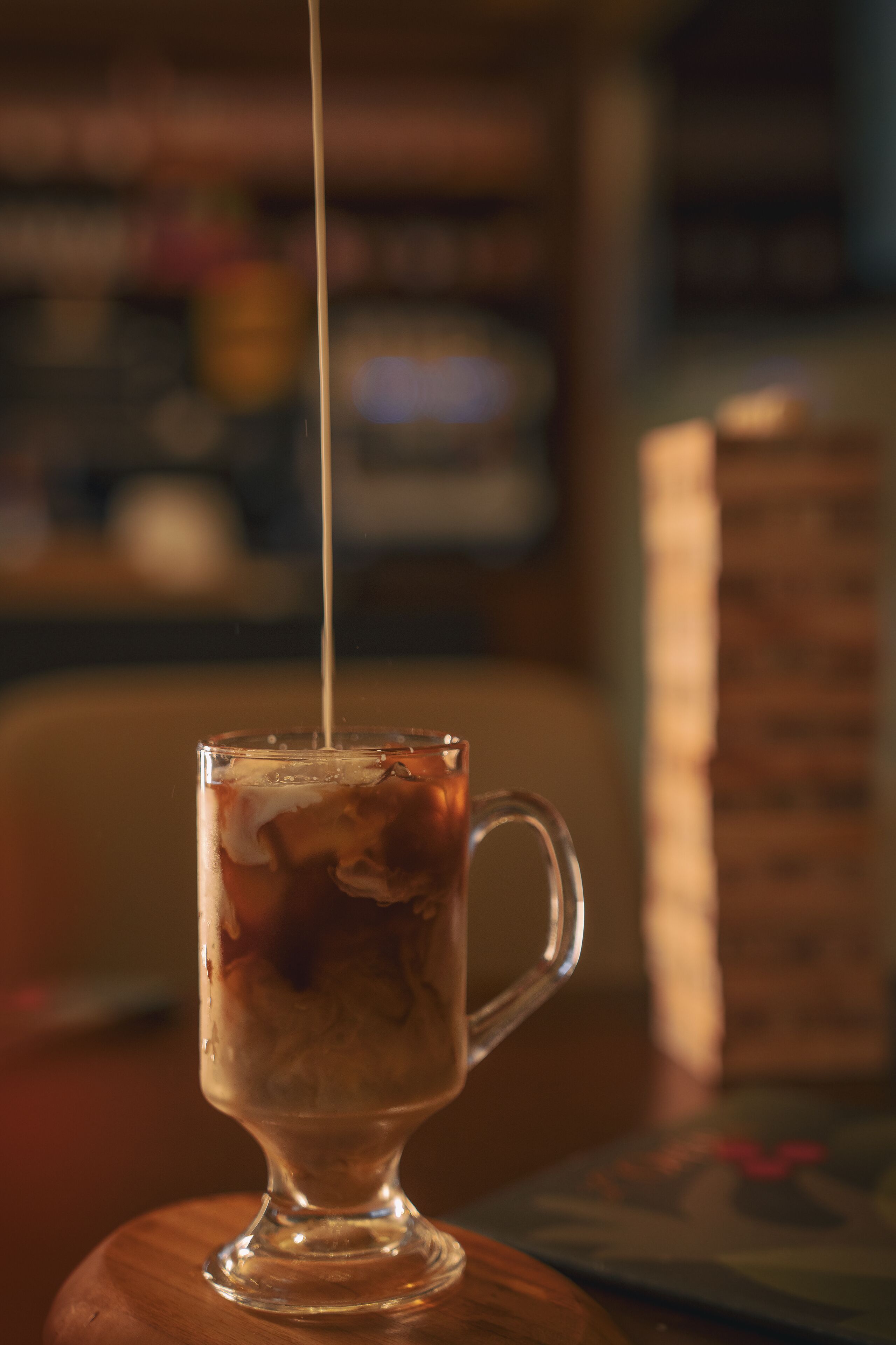 Una taza de vidrio transparente sobre una superficie de madera, con un líquido siendo servido.