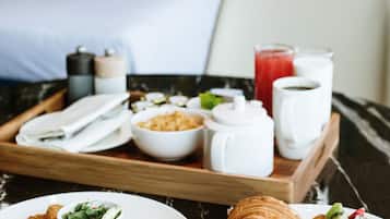 Bandeja de desayuno con cruasanes, tomate a la parrilla y ensalada sobre una mesa de mármol en una habitación de hotel.