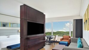 Una habitación de hotel moderna con un televisor de pantalla plana grande, un sofá, una mesa de centro y un área de comedor con una mesa y sillas.