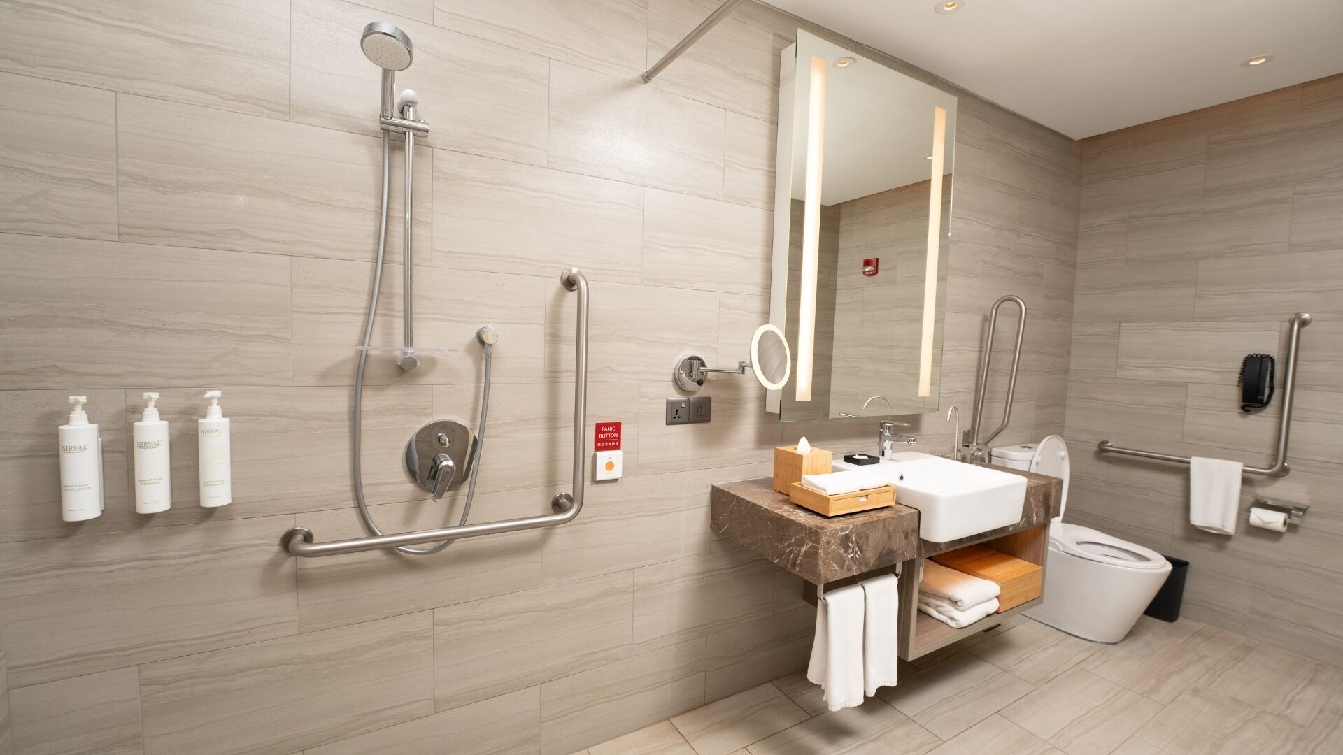 Une salle de bain moderne équipée d’une douche, de barres d’appui, d’un lavabo et de toilettes.