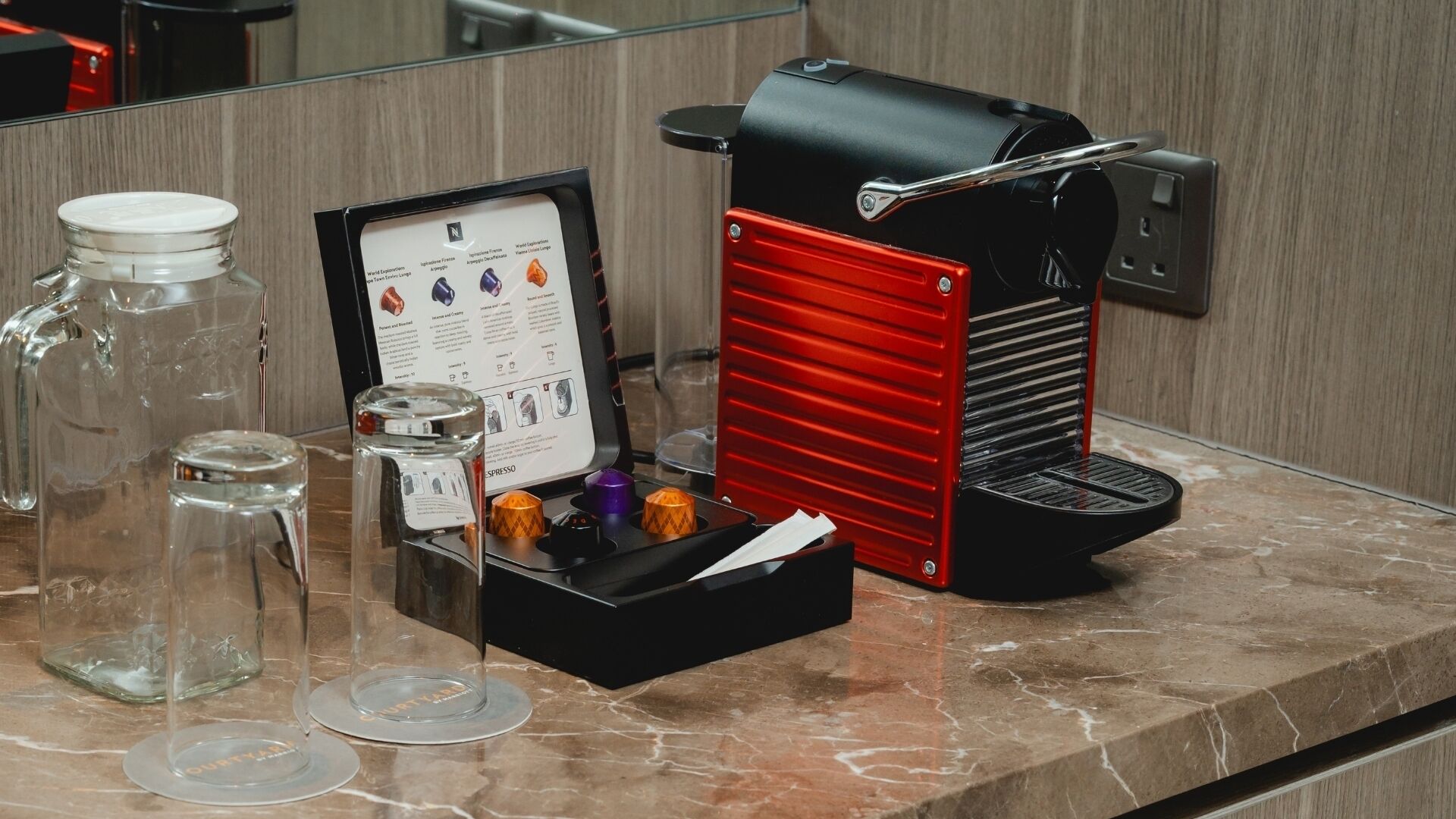 A coffee machine, a menu, and two glass jars on a marble countertop.
