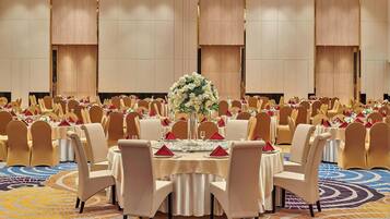 Une salle de banquet avec des tables rondes, des chaises de couleur beige et un tapis à motifs.