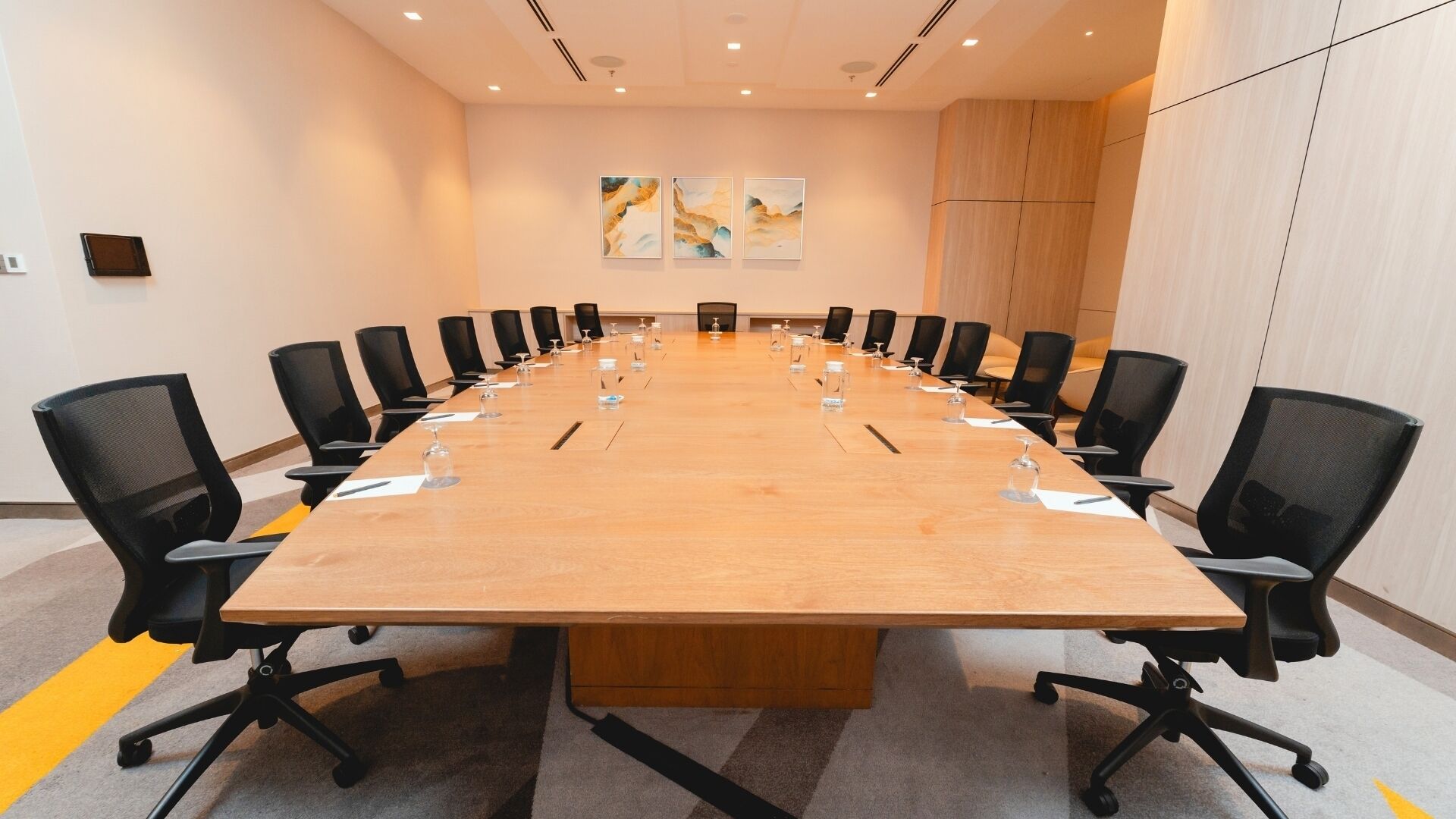 A conference room with a long table, black chairs, and a few paintings on the wall.