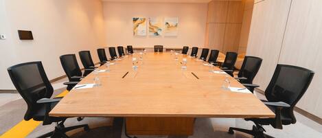 A conference room with a long table, black chairs, and a few paintings on the wall.