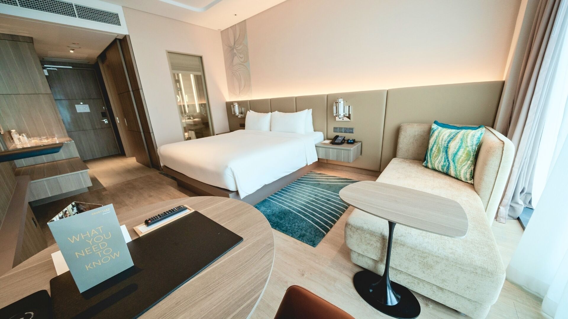 A hotel room with a bed, a desk, a chair, a nightstand, and a bathroom area.