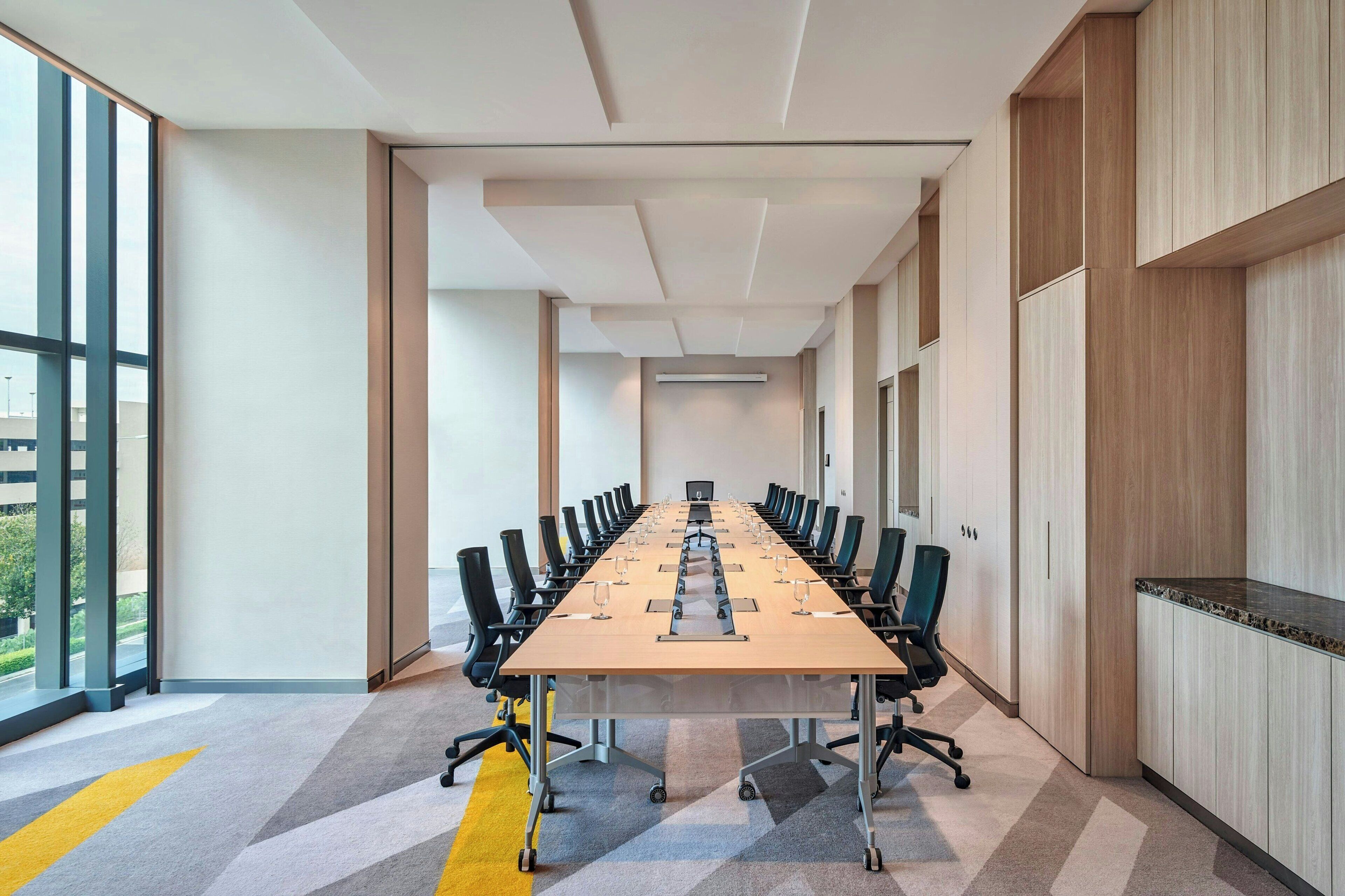 A conference room with a long table, chairs, and a view through large windows.