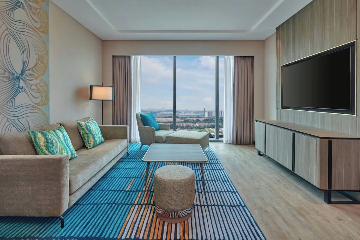 Una habitación de hotel moderna con sofá, reposapiés y televisor de pantalla plana.