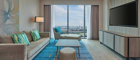 Una habitación de hotel moderna con sofá, reposapiés y televisor de pantalla plana.