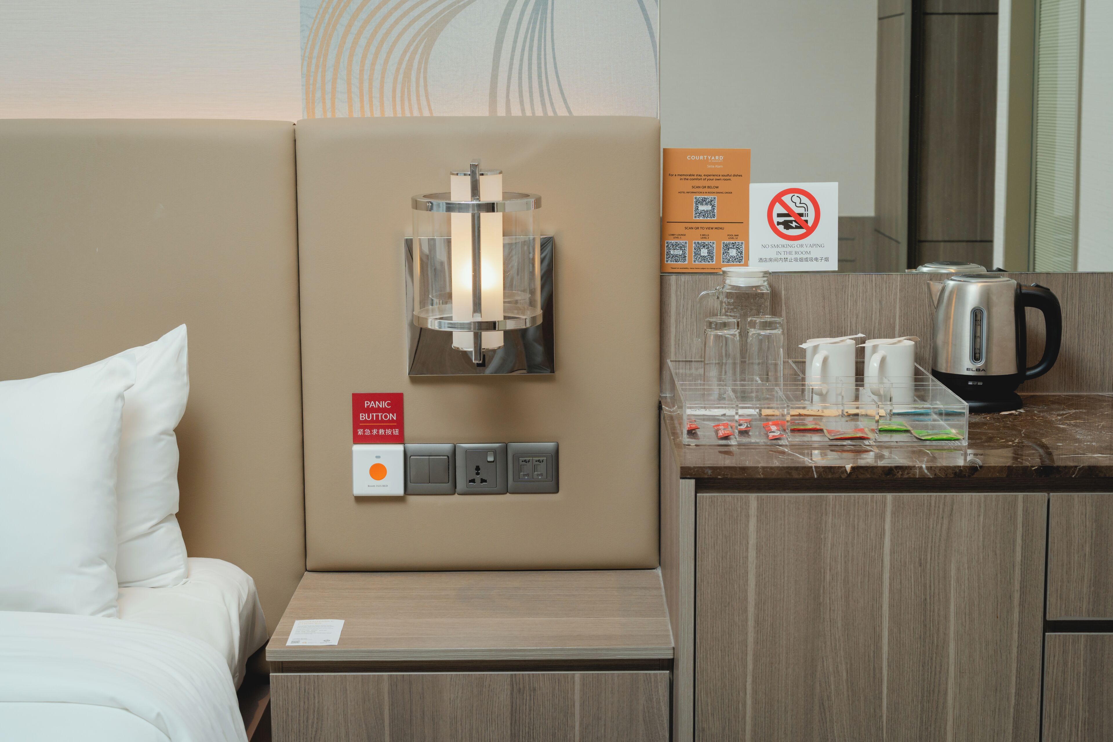 A hotel room with a bed, a wall-mounted light fixture, a minibar, and a no-smoking sign.