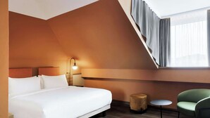 A modern hotel room with a large bed, a small round table, a green chair, and a window with curtains. - June Six Salzburg, a Tribute Portfolio Hotel (Salzburg)