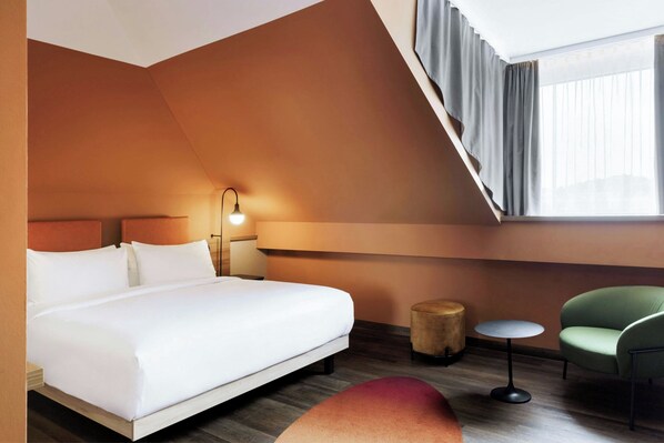 A modern hotel room with a large bed, a small round table, a green chair, and a window with curtains. - June Six Salzburg, a Tribute Portfolio Hotel (Salzburg)