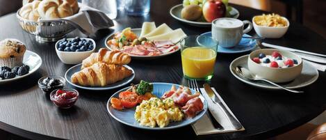 Una mesa de desayuno con cruasanes, huevos, tomates y varias frutas.