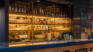 A bar area with shelves of liquor bottles and glasses, a cash register, and bar stools. - June Six Salzburg, a Tribute Portfolio Hotel (Salzburg)