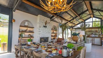A spacious dining area with a large wooden table and chairs, a chandelier, and a kitchen in the background.
