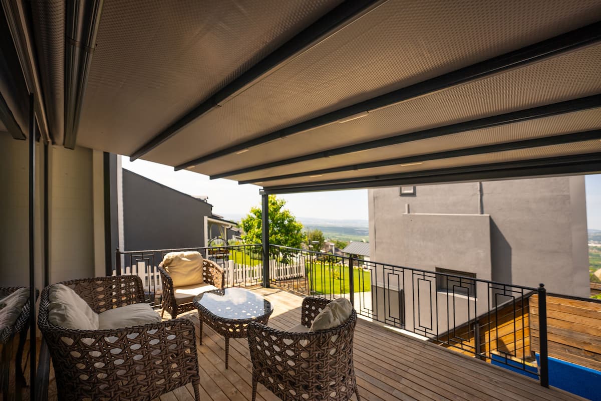 A covered outdoor area with wicker furniture and a view of a modern building and landscape.