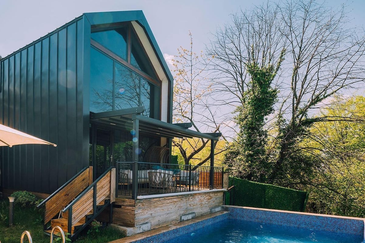 A modern house with a pool, wooden deck, and a covered patio area.