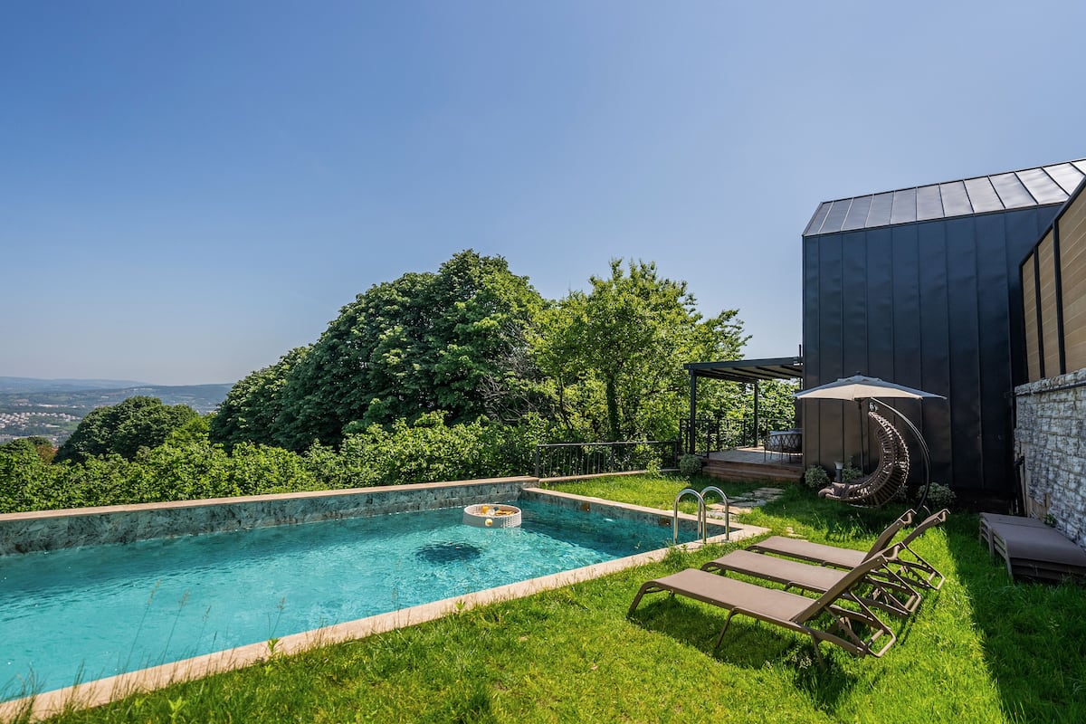 A swimming pool with a view of the countryside, surrounded by lush greenery and a modern building.