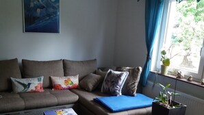Ein Wohnzimmer mit einer Couch, einem Hocker, einem Couchtisch und einer Topfpflanze.